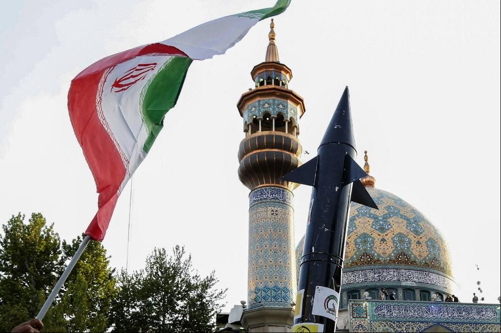Iranianos levantam uma bandeira e a maquete de um míssil durante uma celebração após o ataque de mísseis e drones do Irã a Israel